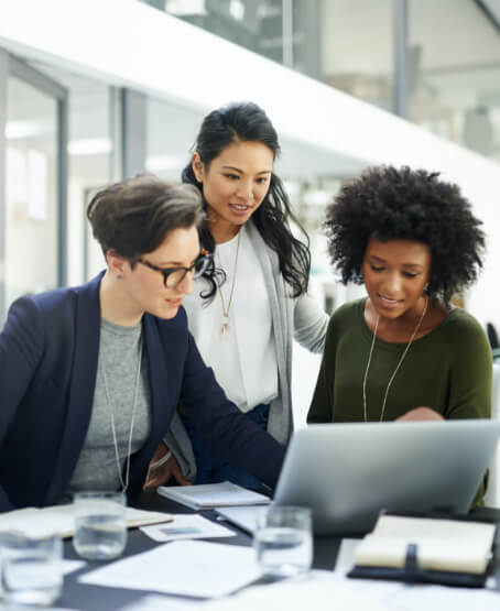 a group of female colleagues in an office looking at a laptop